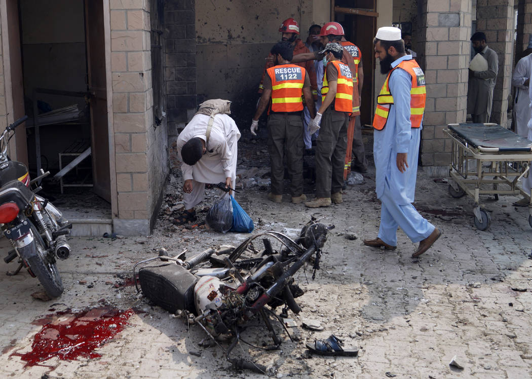 Pakistani security officials and rescue workers gather at the site of a bombing on an entrance ...