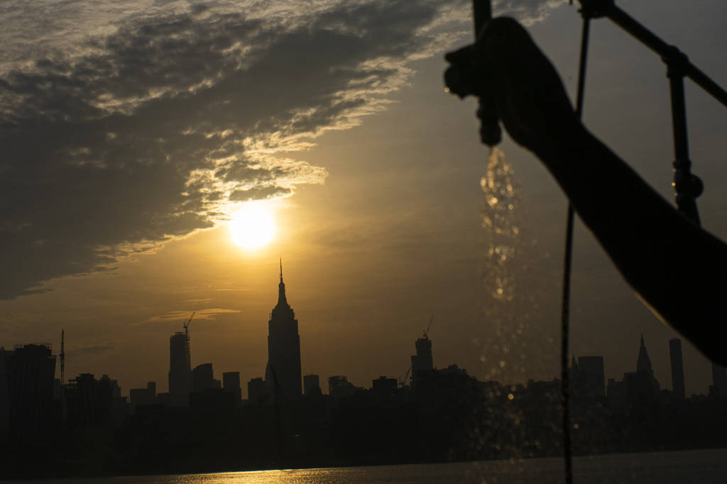 The sun rises over New York City and the Empire State Building while a man sprays water at Pier ...