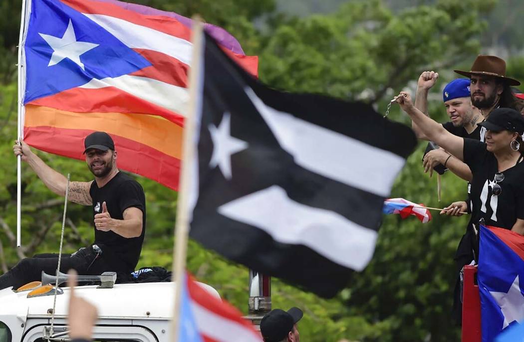 Ricky Martin, holding a Puerto Rican flag and a rainbow banner, flashes a thumbs up as he joins ...