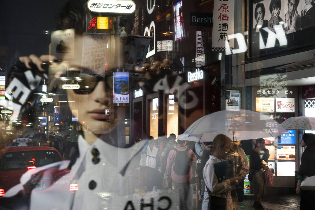 Pedestrians are seen through an advertisement as they walk along the busy streets of the Shibuy ...