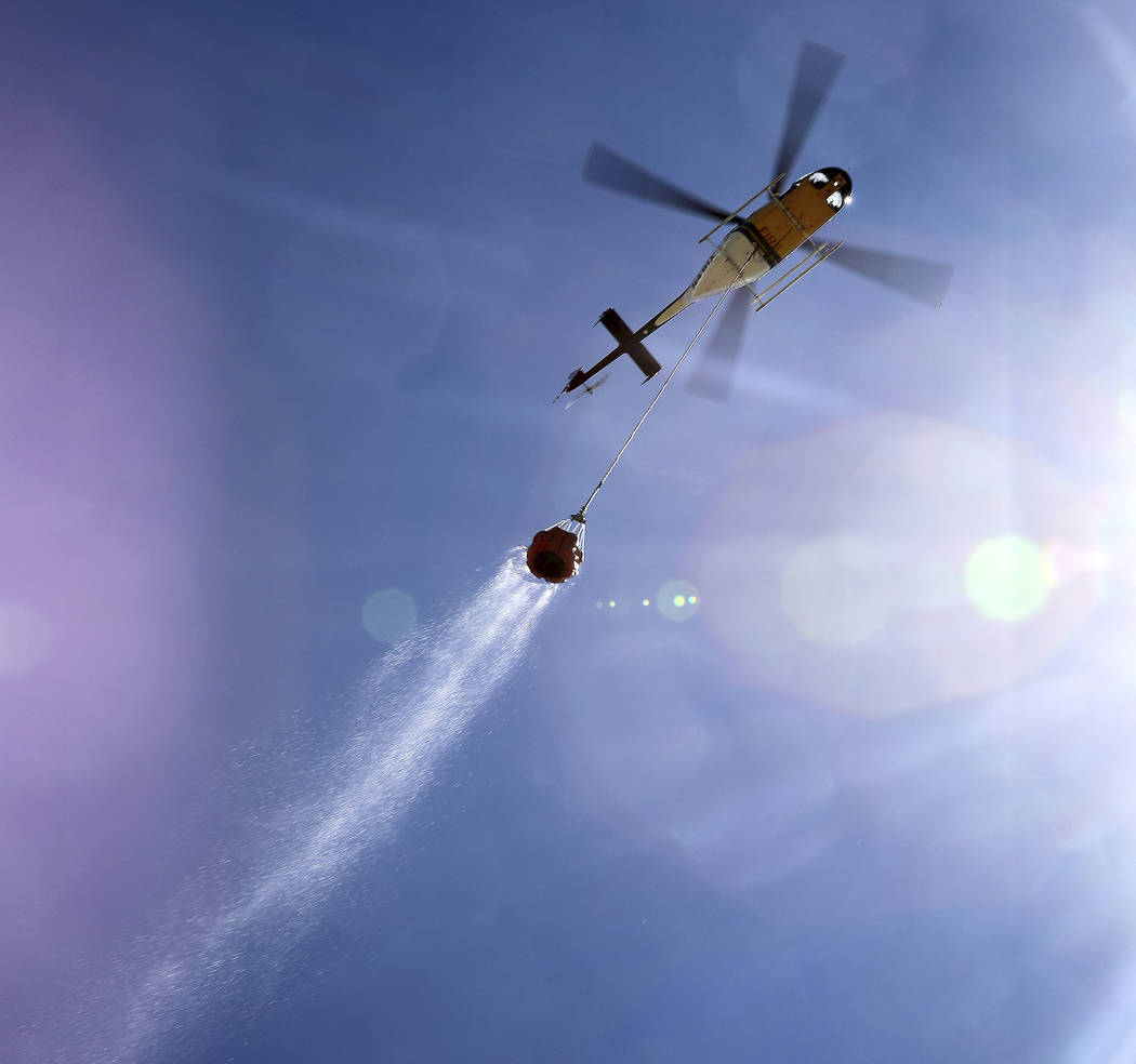 A helicopter drags a Bambi Bucket full of water through the sky on it's way to quench hot spots ...