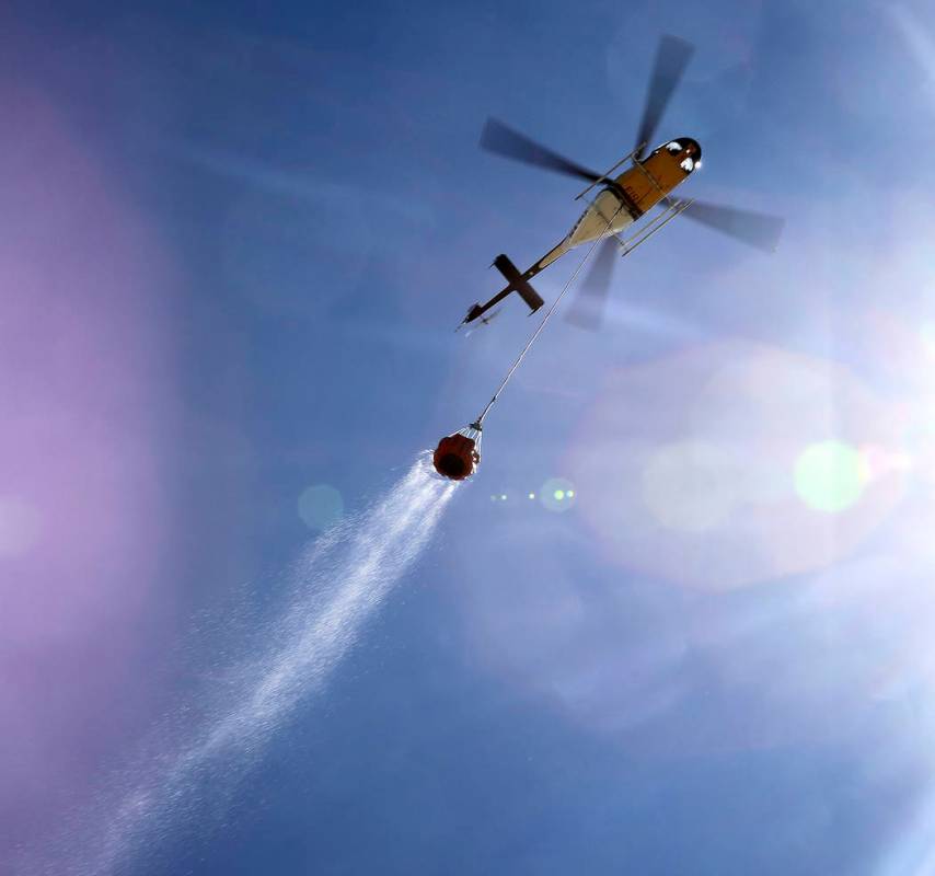 A helicopter drags a Bambi Bucket full of water through the sky on it's way to quench hot spots ...