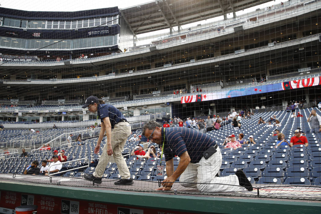 Workers adjust new netting that separates the infield from lower bowl seating before a pos ...