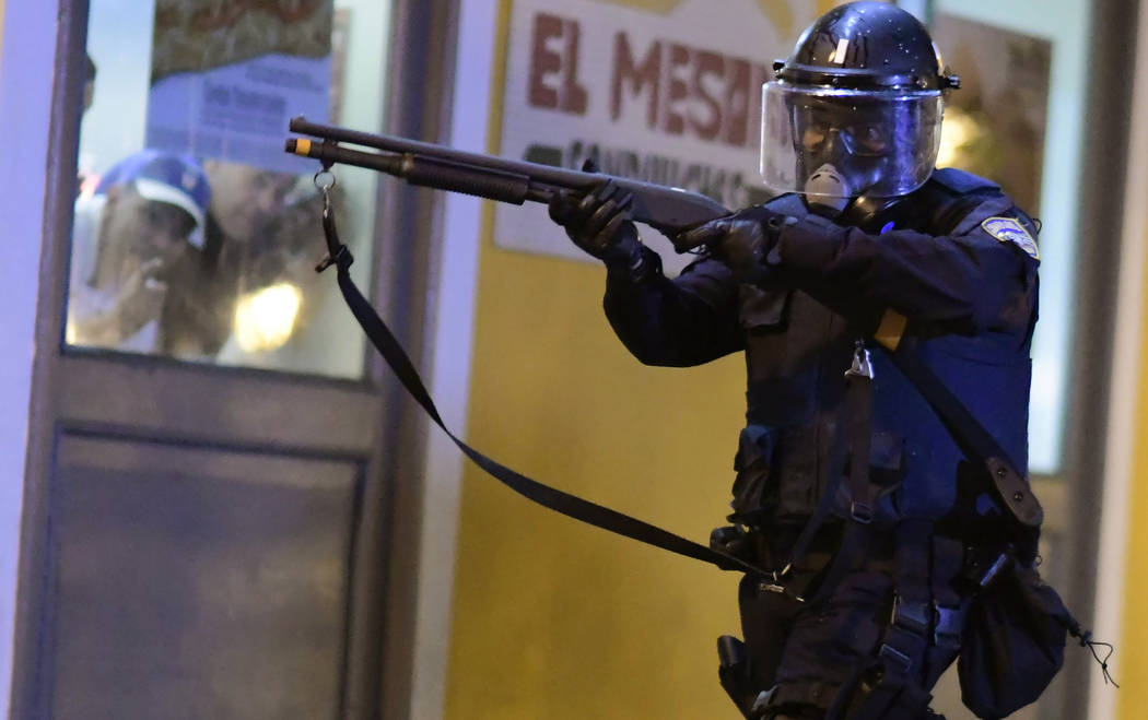 A member of the riot control units patrol the street while people look out the window during cl ...