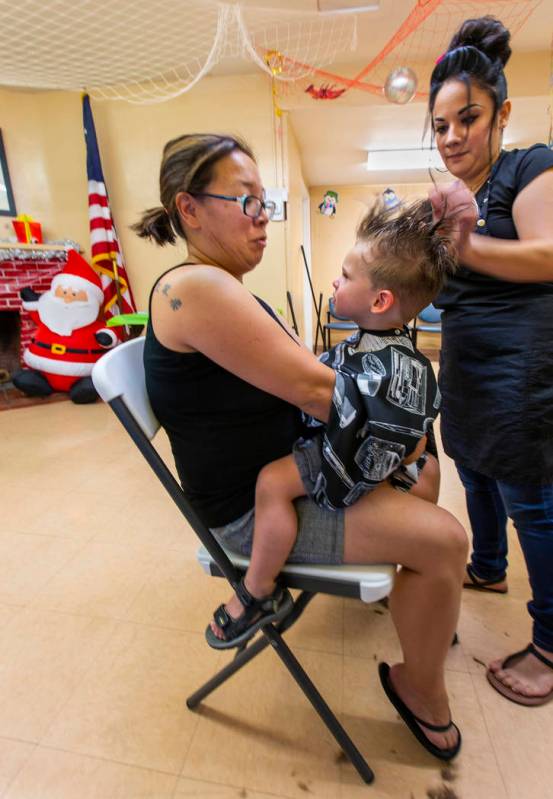 Soon Lewis, left, holds son Anderson, 2, as he receives his haircut from stylist Heather Delgad ...