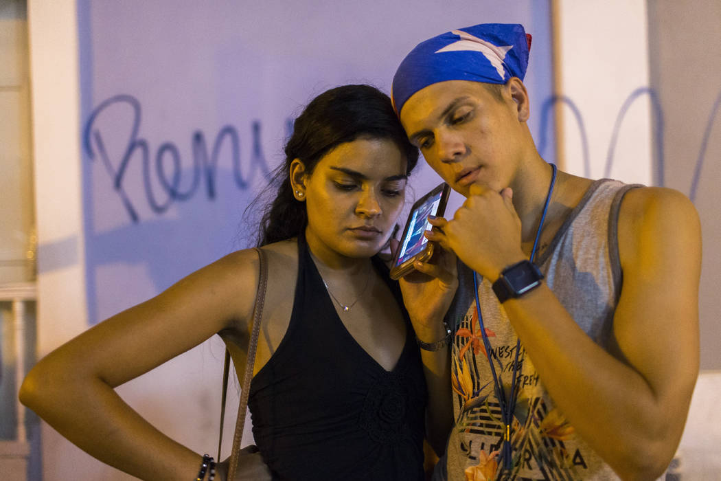 Locals listen on a smart phone to the pre-recorded message by Puerto Rico Gov. Ricardo Rossello ...