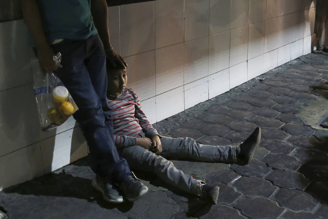 In this July 18, 2019 photo, a migrant child and his father stay together after being bused by ...