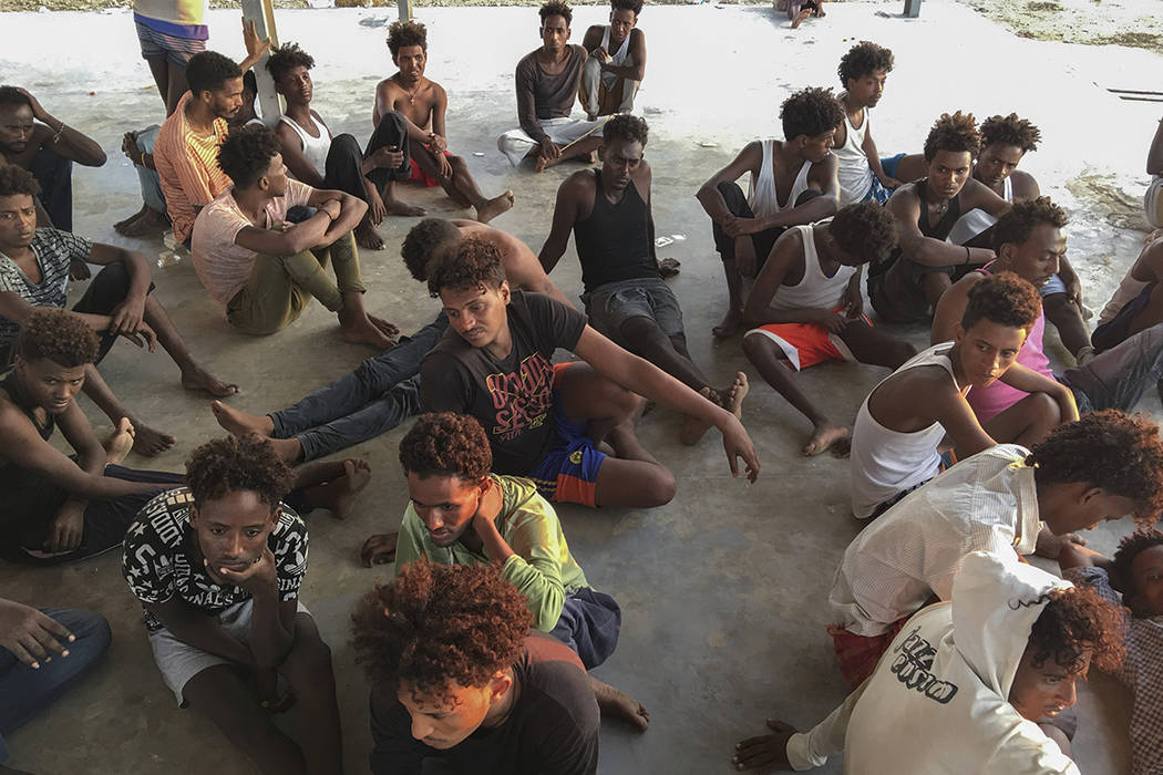 Rescued migrants sit on a coast some 100 kilometers (60 miles) east of Tripoli, Libya, Thursday ...