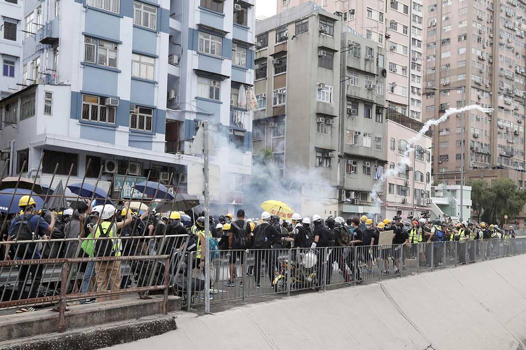 Protesters react to tear gas as they face off with riot police at the entrance to a village at ...