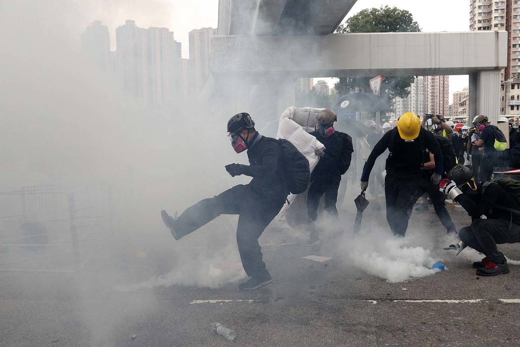 Protesters kick back and pick up tear gas canisters during a face off with riot police at Yuen ...