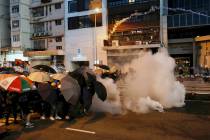 Protesters use umbrellas to shield themselves from tear gas fired by policemen as they face off ...