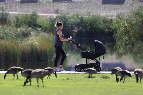 A woman pushes a baby in a stroller as she walks at Cornerstone Park during a hot morning on Mo ...