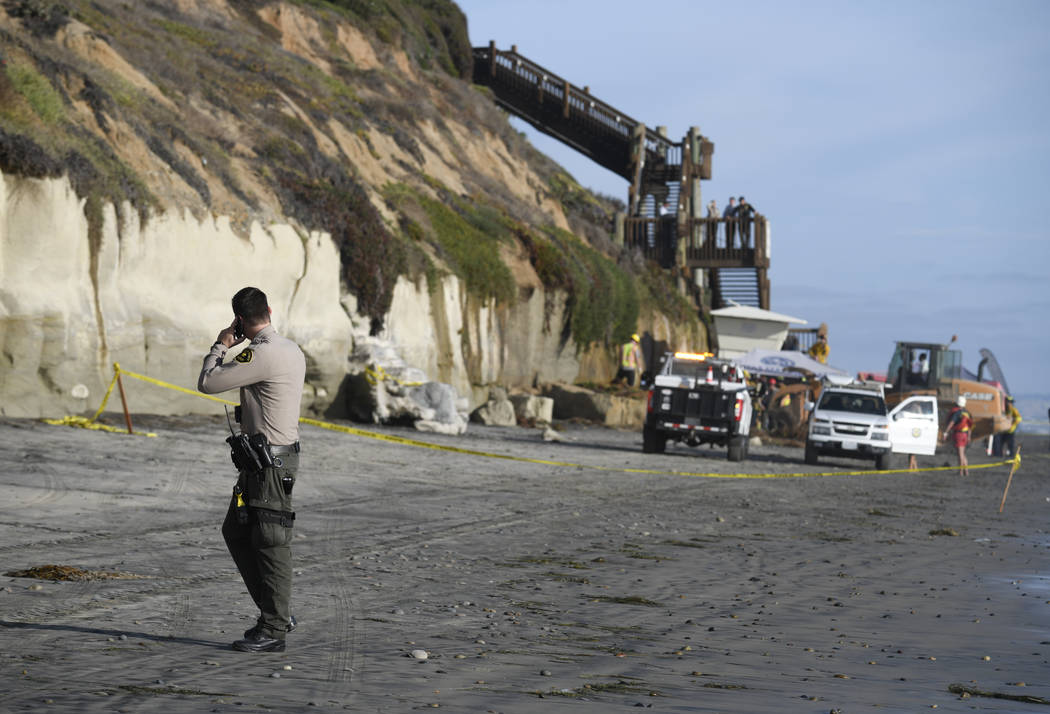 A San Diego County Sheriff's deputy looks on as search and rescue personnel work at the site of ...