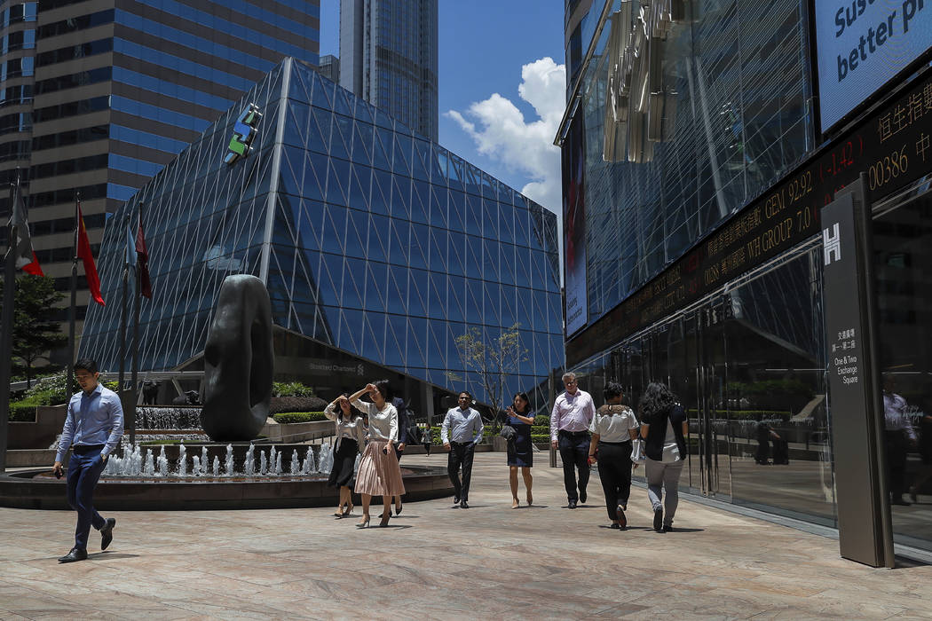 Office workers walk past an electronic board showing shares prices at the financial district in ...