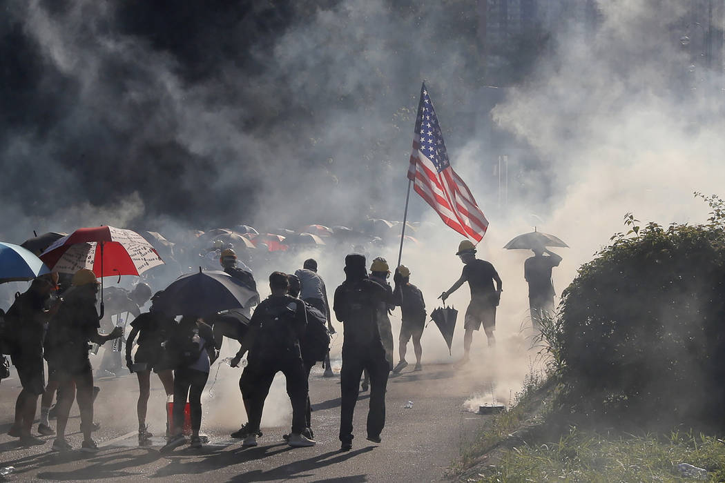 A protester runs with a United States flag as tear gas are released on protesters in Hong Kong ...