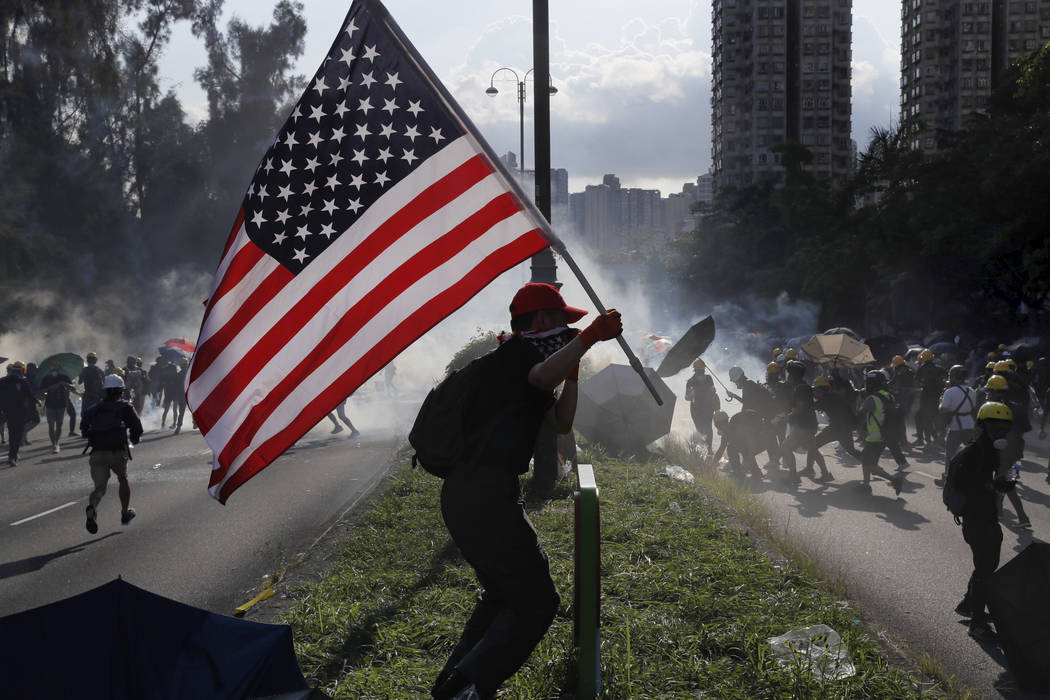 A protester runs with a United States flag as tear gas are released on protesters in Hong Kong ...