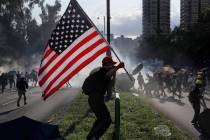 A protester runs with a United States flag as tear gas are released on protesters in Hong Kong ...