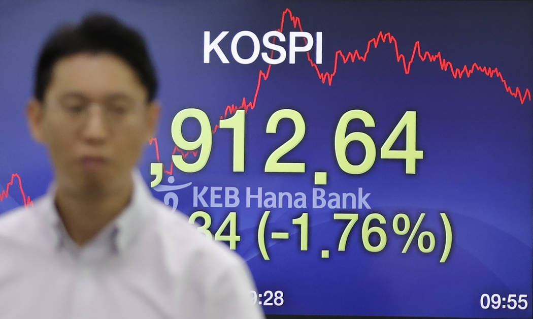 A currency trader walks by the screen showing the Korea Composite Stock Price Index (KOSPI) at ...