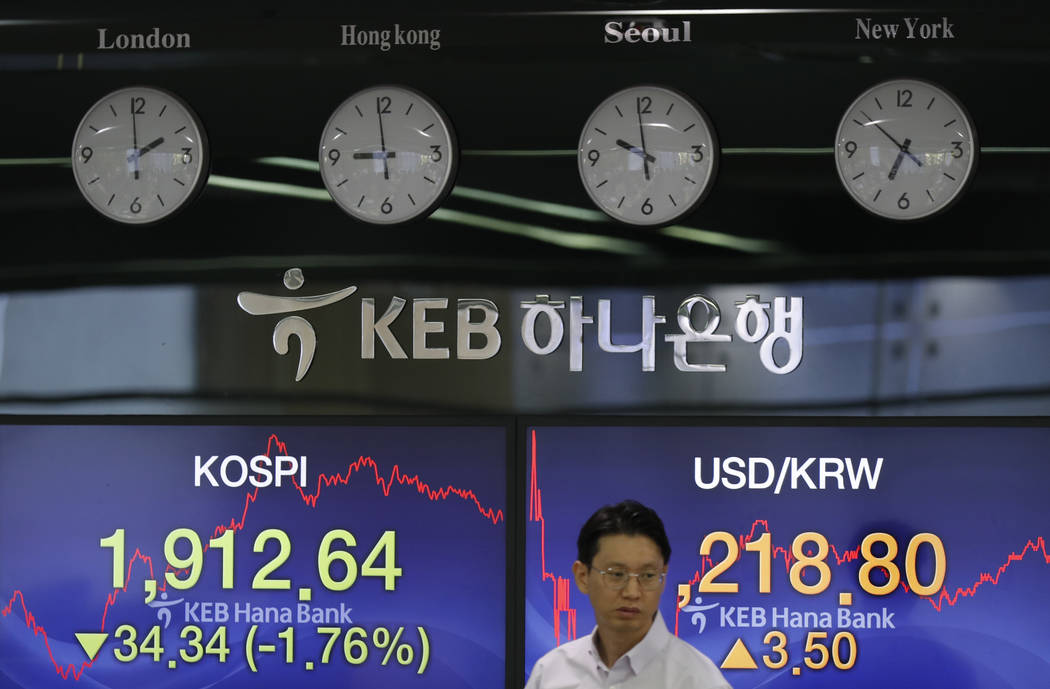 A currency trader walks by the screens showing the Korea Composite Stock Price Index (KOSPI), l ...