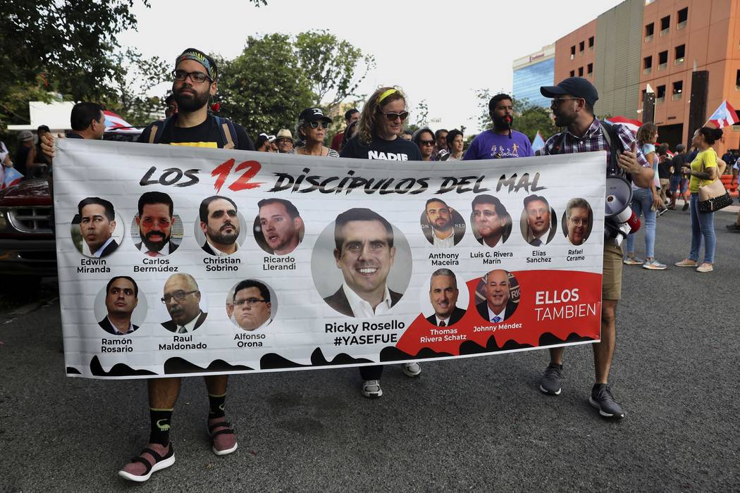 Protesters hold a banner featuring resigned Gov. Ricardo Rosselló, center, amid other poli ...