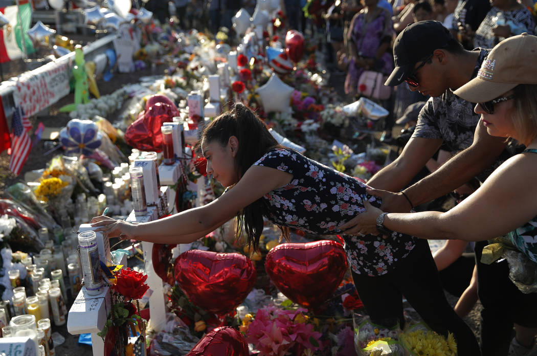 A woman leans over to write a message on a cross at a makeshift memorial at the scene of a mass ...