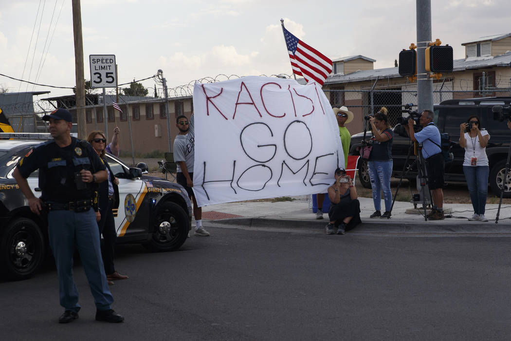 Demonstrators hold a sign as the motorcade carrying President Donald Trump arrives to visit a j ...