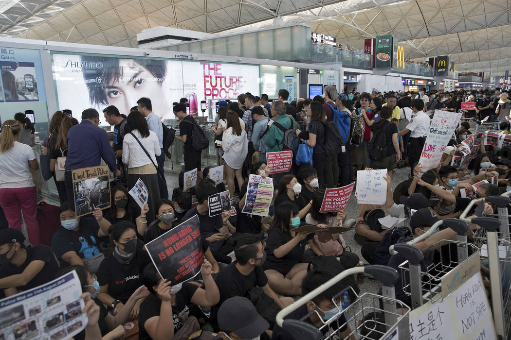 Travelers walk past as protesters hold a sit-in rally near the departure gate of the Hong Kong ...