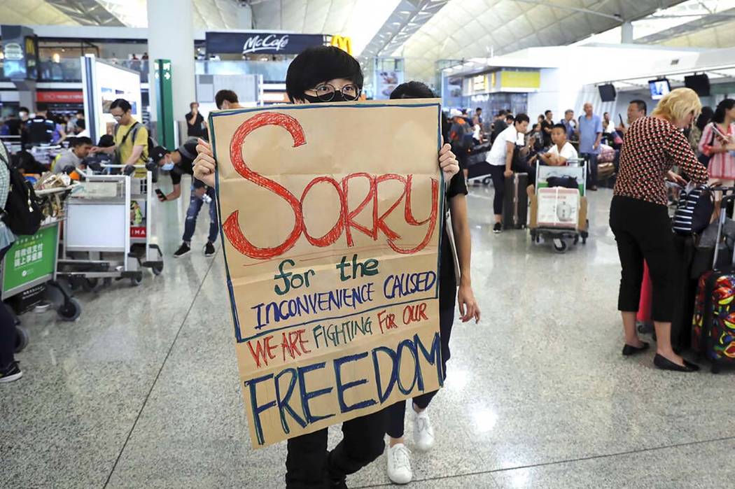 A protester shows a placard to stranded travelers during a demonstration at the Airport in Hong ...