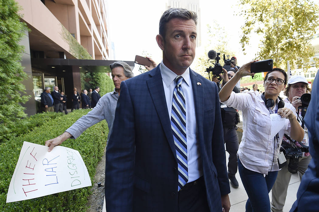 U.S. Rep. Duncan Hunter, center, leaves an arraignment hearing as a protester carries a sign, l ...