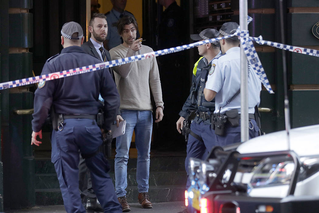 A man, center, points as he assists police at a building where a person has been found deceased ...