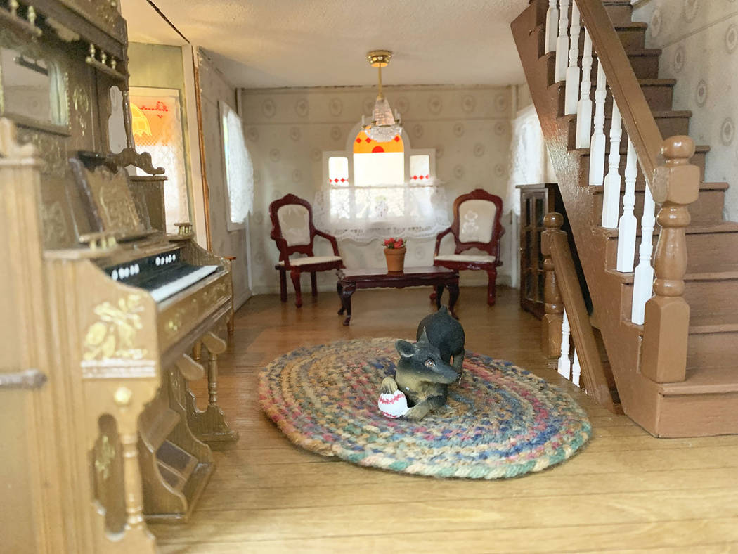 On the first floor of the dollhouse, a model dog sits in the middle of the room playing beside ...