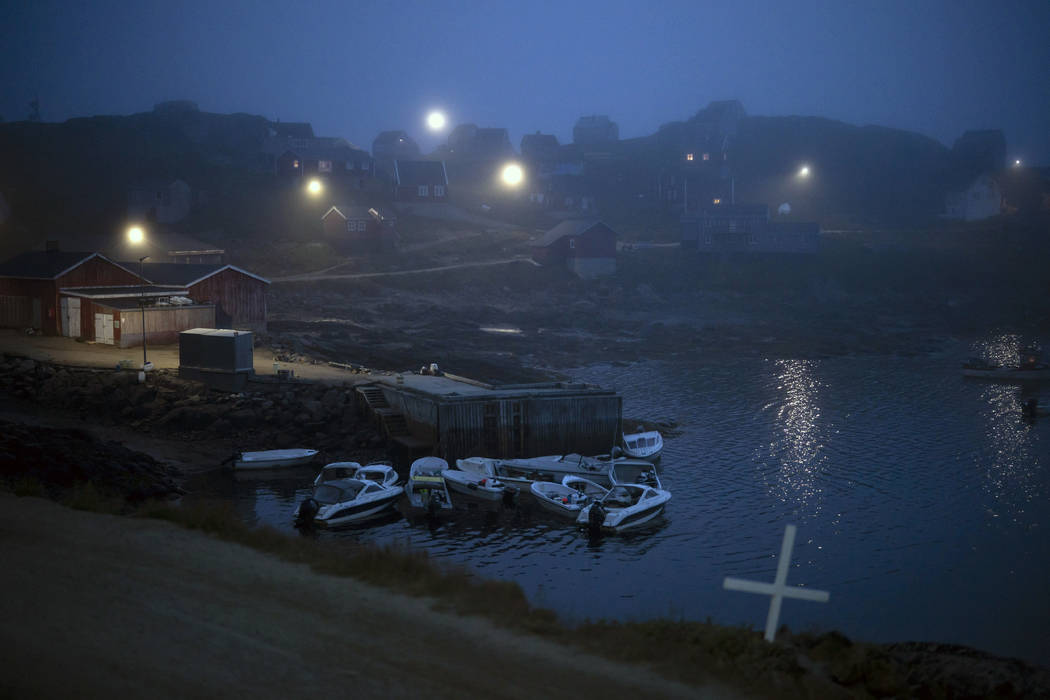 A cross sits on the side of the road as fog covers homes in Kulusuk, Greenland, early Thursday, ...