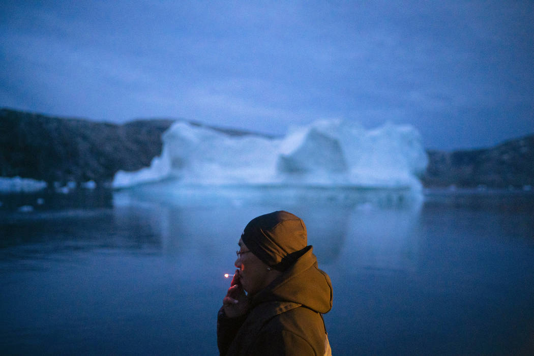 A local man smokes a cigarette as he rides on a boat past icebergs in eastern Greenland, late F ...