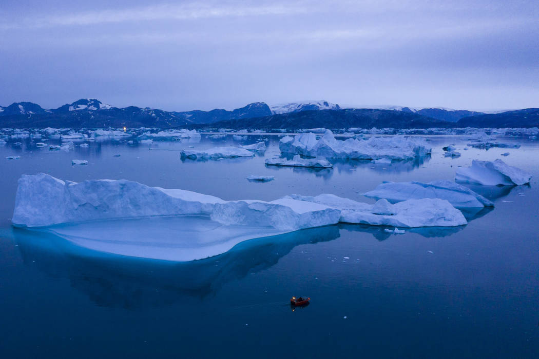 In this Aug. 15, 2019, photo, a boat navigates at night next to large icebergs near the town of ...