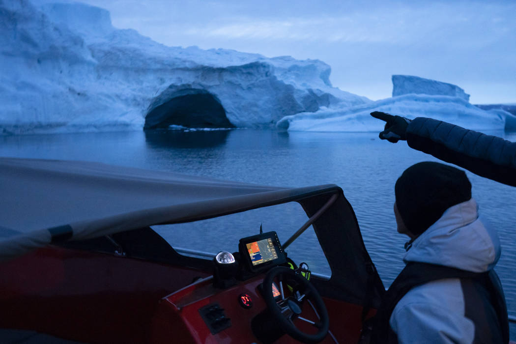 In this Aug. 16, 2019, photo, a boat navigates at night next to a large iceberg in eastern Gree ...