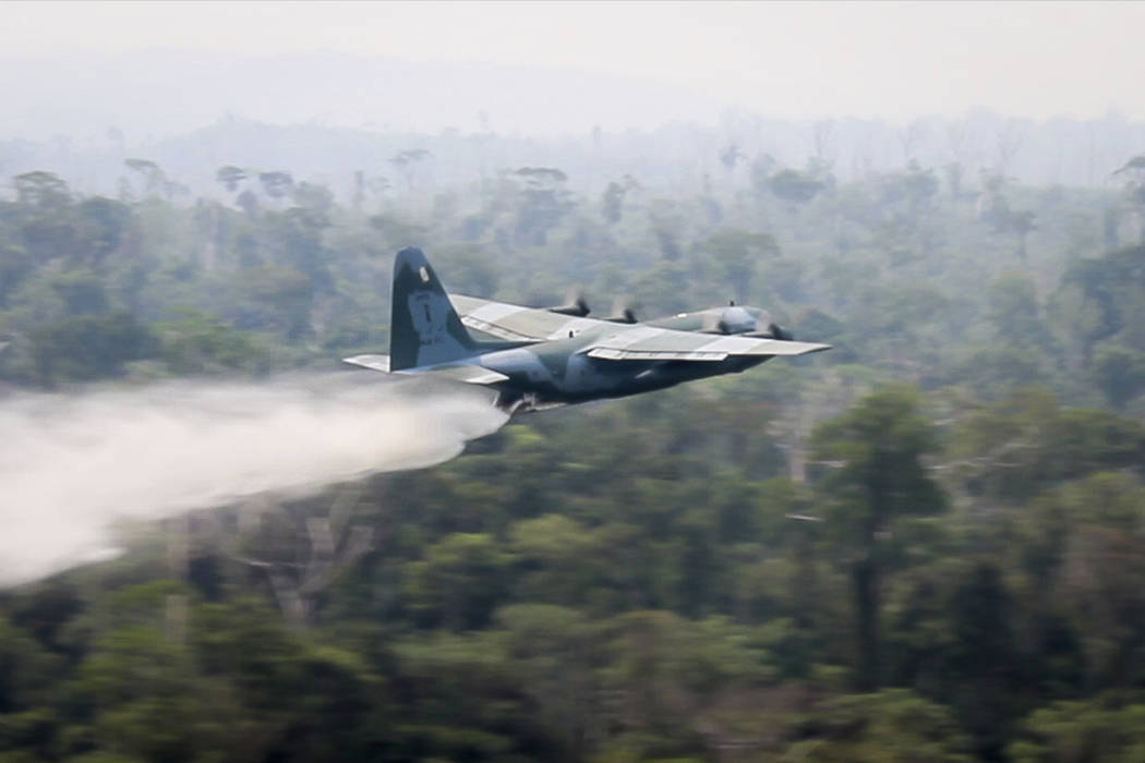 In this photo released by Brazil Ministry of Defense, a C-130 Hercules aircraft dumps water to ...