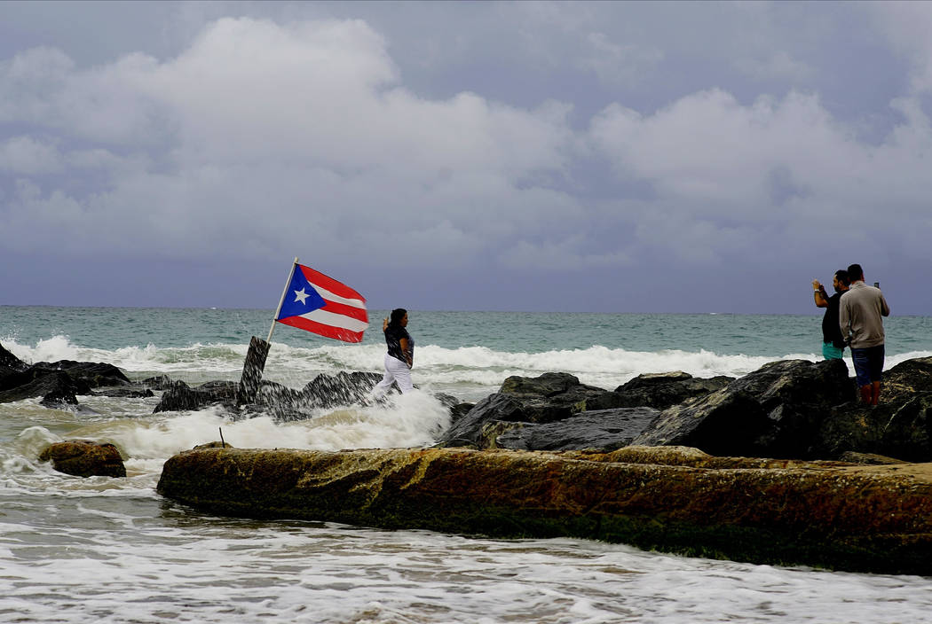 A woman poses for a photo backdropped by ocean waters and a Puerto Rican national flag, after t ...