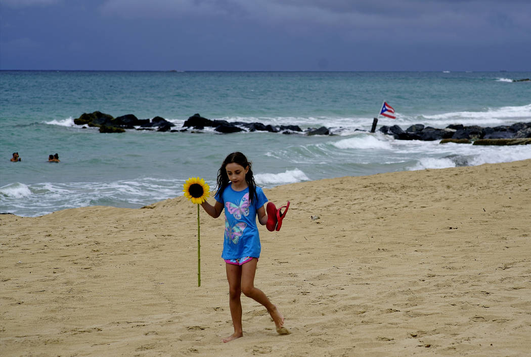 A girl walks on a sandy beach holding a sunflower and her flip flops after the passing of Tropi ...