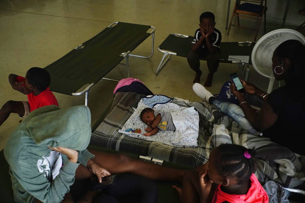 Anastacia Makey, 43, far right, looks at her phone as she and her family sits on cots with othe ...