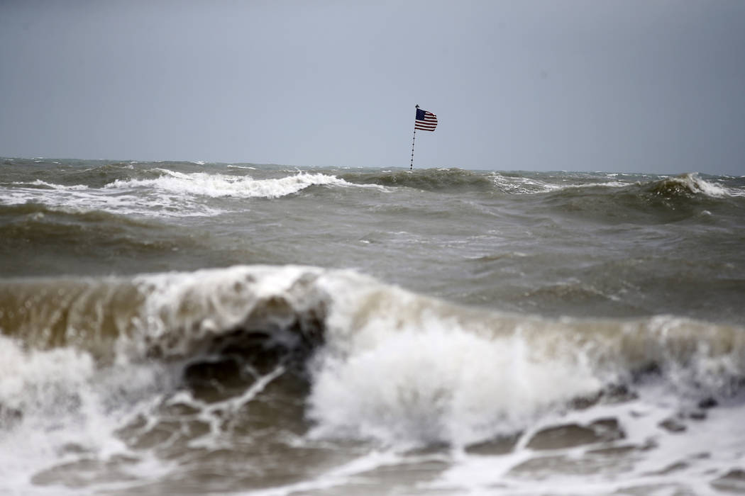 Waves crash in front of an American flag that is planted on a jetty during a high surf from the ...