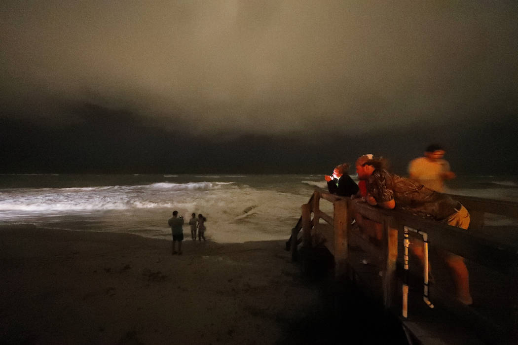 People stand on the boardwalk along the Atlantic Ocean at night as the outer bands of Hurricane ...