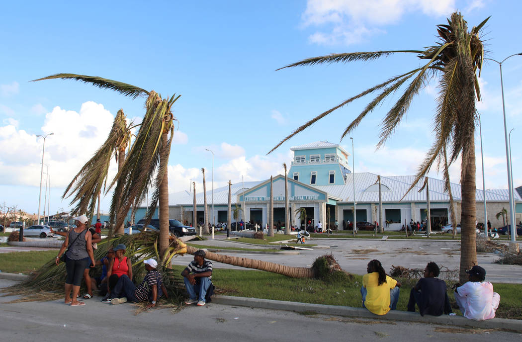 People sit under broken palm trees outside the Leonard M. Thompson International Airport after ...