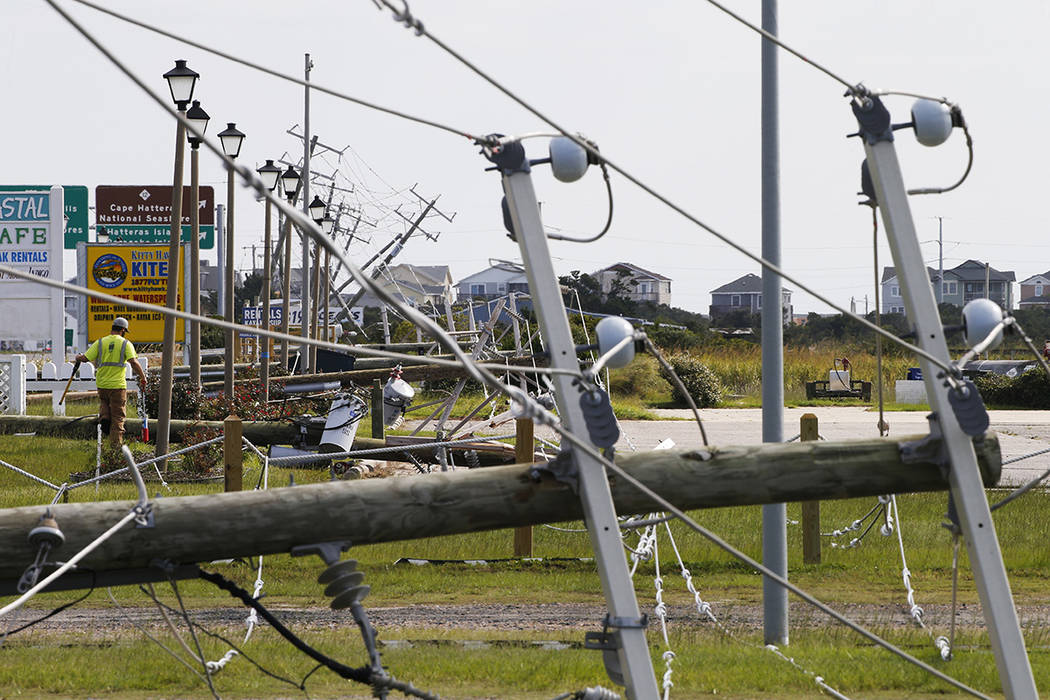 A utility worker walks through downed power lines along a causeway in Nags Head, NC., Saturday, ...