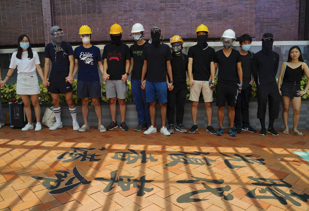 Students from Hong Kong University join their hands and shout slogans near Chinese calligraphy ...