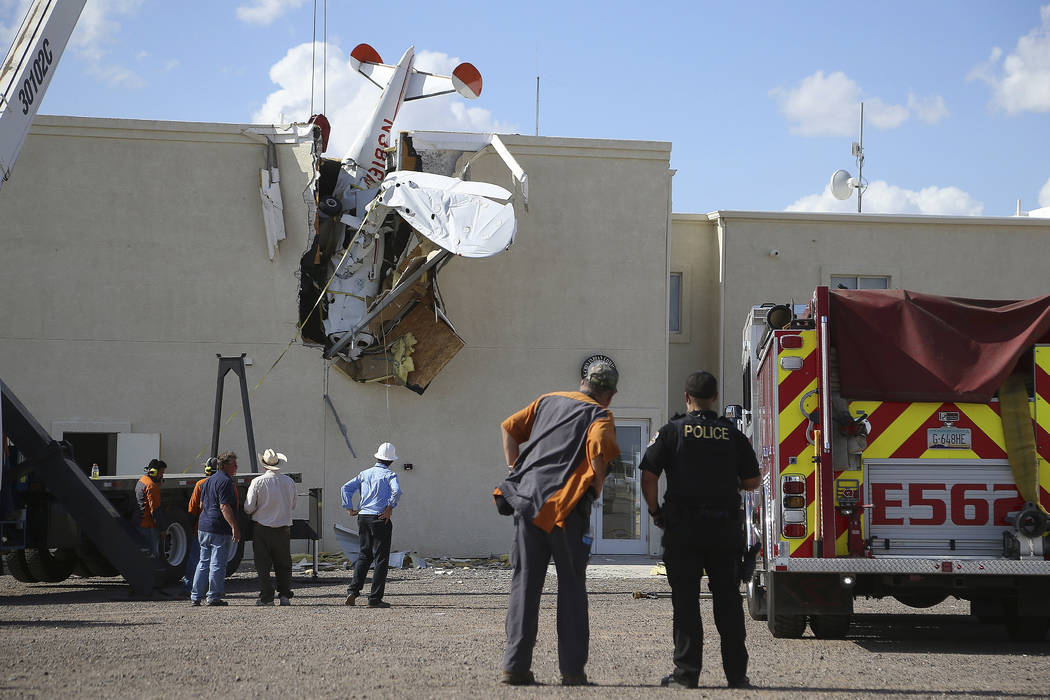 Police and fire personnel look on as workers remove a single-engine plane after it crashed into ...