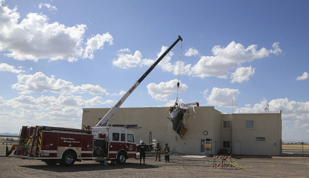 As fire personnel look on, workers remove a single-engine plane after it crashed into the termi ...