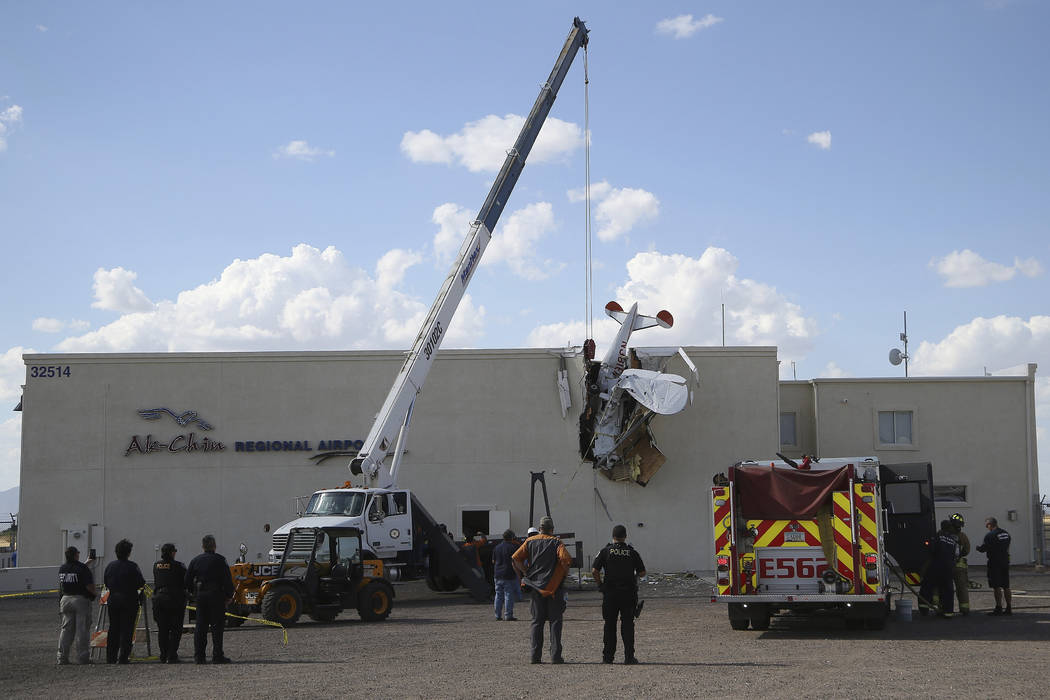 Police and fire personnel look on as workers remove a single-engine plane after it crashed into ...