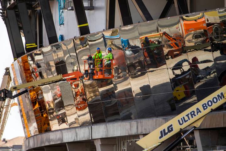 Crews work to install glass panes along the lower lever of Allegiant Stadium on Tuesday, Sept. ...