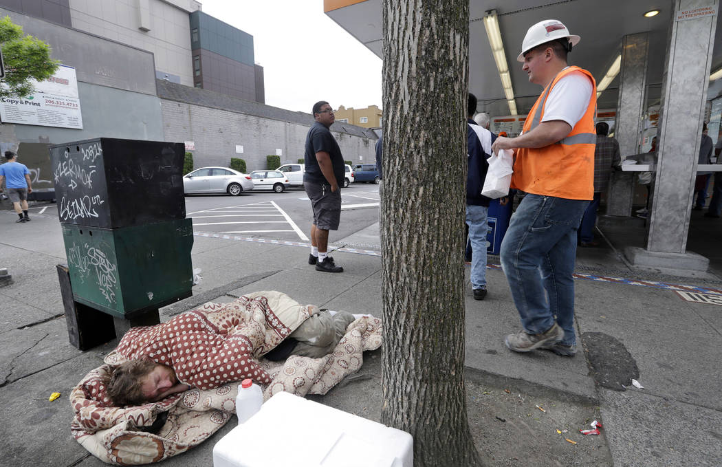 FILE - In this May 24, 2018 file photo, a man sleeps on the sidewalk as people behind line up t ...