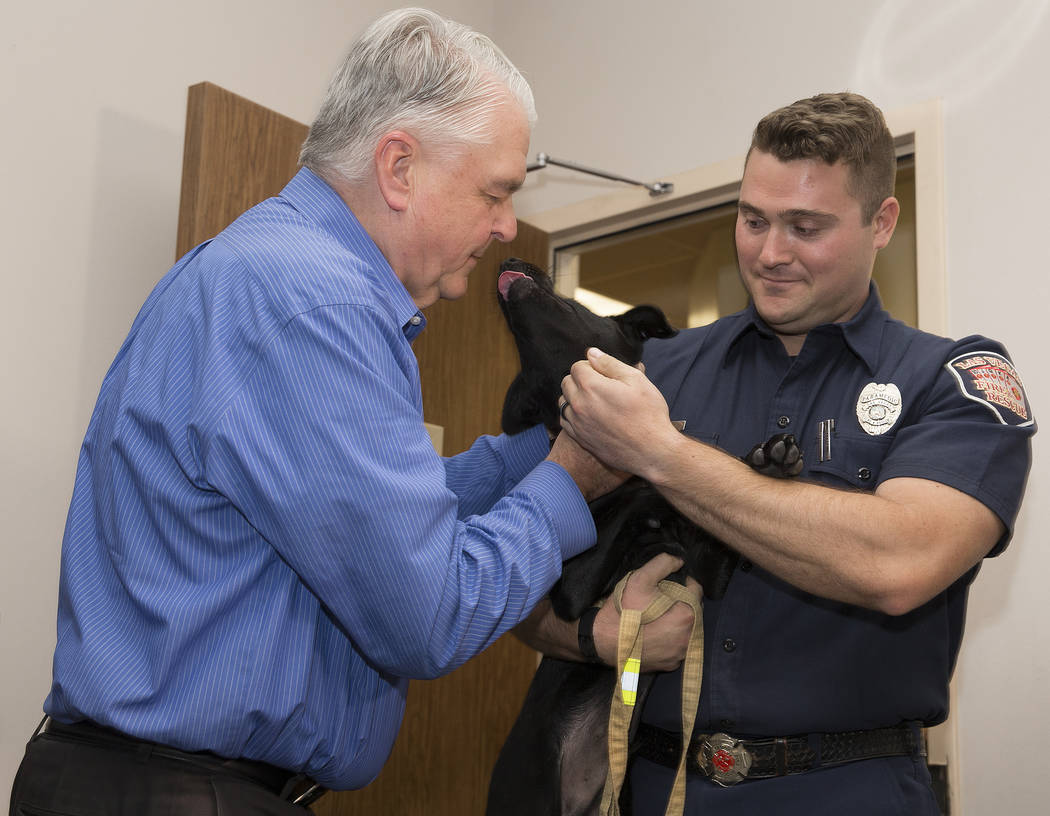Gov. Steve Sisolak, left, pets a black lab puppy named Blaze, held by Las Vegas Fire and Rescue ...